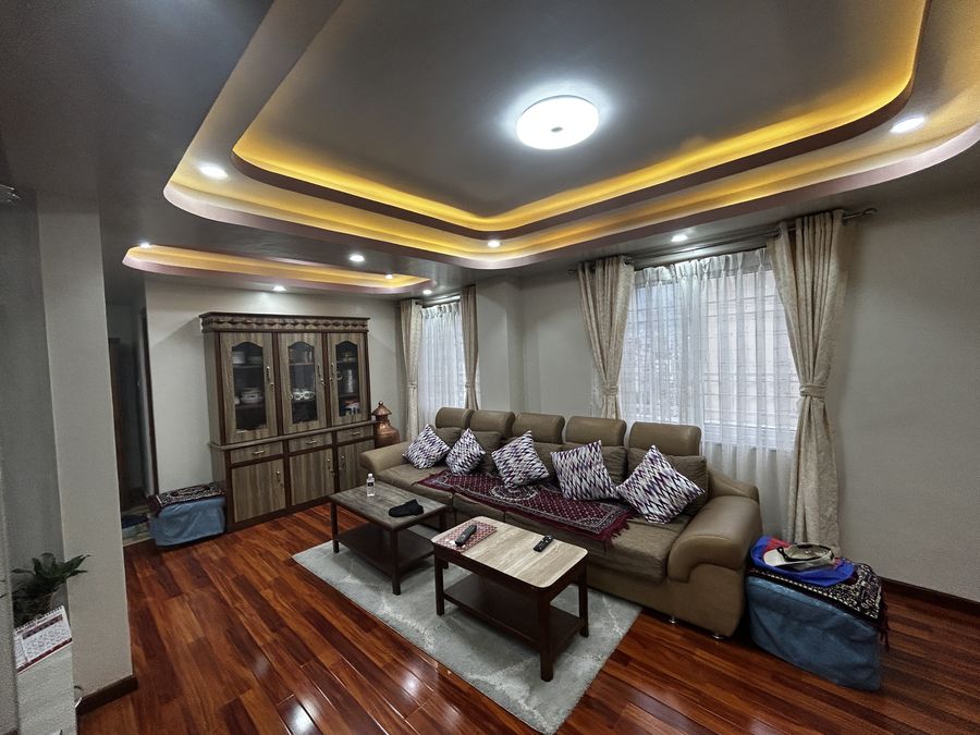 Living room of Ruku Gurung House with a cove-lit false ceiling, timber-look flooring and a corner sofa