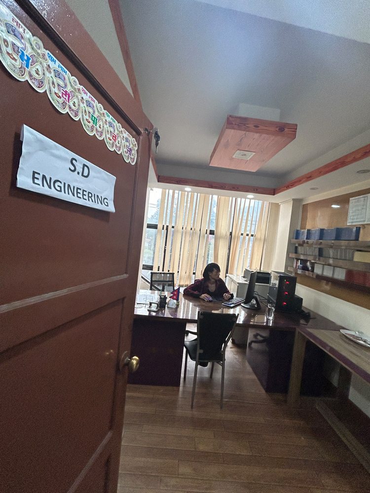 The S.D Engineering office door, open onto a room where two staff work at desks lined with drawing files